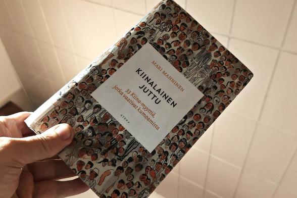 Kirja kädessä. Kannessa piirroskuva väkijoukosta ja sen päällä keskellä laatikko, jossa kirjan tekijä ja nimi.