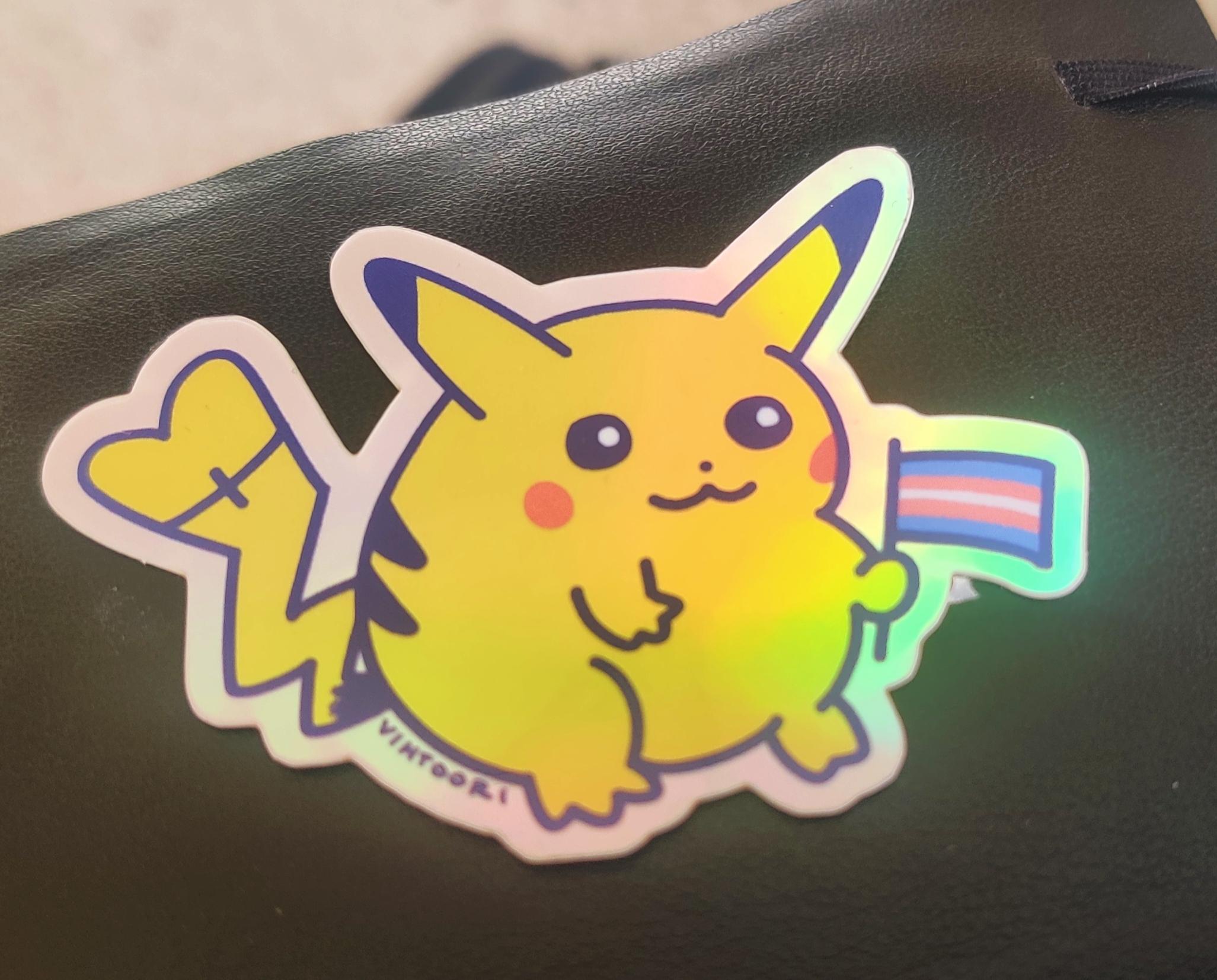 A shining Pikachu sticker with a chonky Pikachu holding a trans flag. Sticker has creator signature Vihtoori.