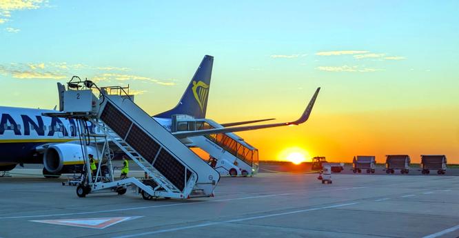 A plane stands on the runway at sunset, the passenger stairs and baggage carts are ready, while the colors of the sunset at the airport tint the sky.

Ein Flugzeug steht bei Sonnenuntergang auf der Startbahn, die Passagiertreppen und Gepaeckwagen stehen bereit, waehrend die Farben des Sonnenuntergangs am Flughafen den Himmel faerben.