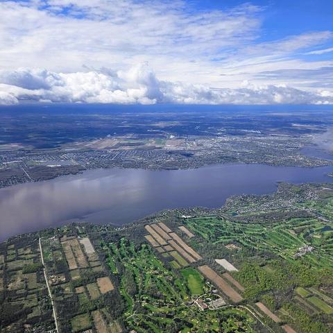 Looking down from plane at a bank of clouds, patchwork of fields and large waterbody.