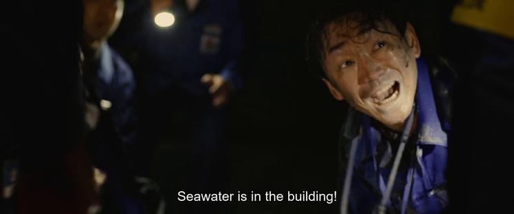A few wet people in blue coveralls, bent over, with flashlights in a dark room. One is yelling. A subtitle reads "Seawater is in the building!"