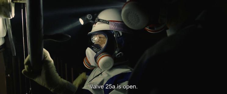 Two workers in protective white suits, helmets and filter masks. The scene is dark, only illuminated by a headlamp on the person holding a large valve. The subtitle reads "Valve 25a is open."