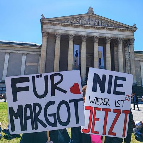 Foto von zwei Demoschildern vor der Glyptothek auf dem Königsplatz.
Text:  FÜR MARGOT ❤️
und:  NIE WIEDER IST JETZT