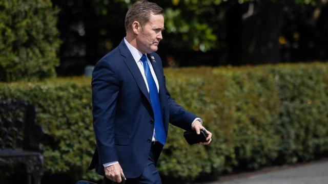 National Security Adviser Michael Waltz walks outside while carrying a briefcase in one hand and a phone in the other.