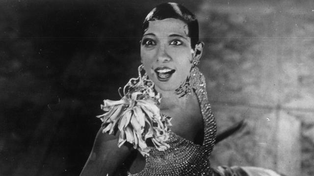 Josephine Baker schaut in ihrem Bühnenoutfit überrascht in die Höhe. Josephine Baker schaut in ihrem Bühnenoutfit überrascht in die Höhe.