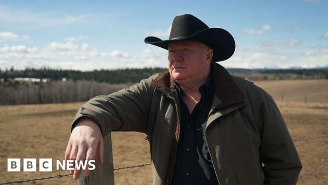 Jeff Rath, a rancher wearing a cowboy hat, leans on a fence post and stares out at the wide open spaces in Alberta