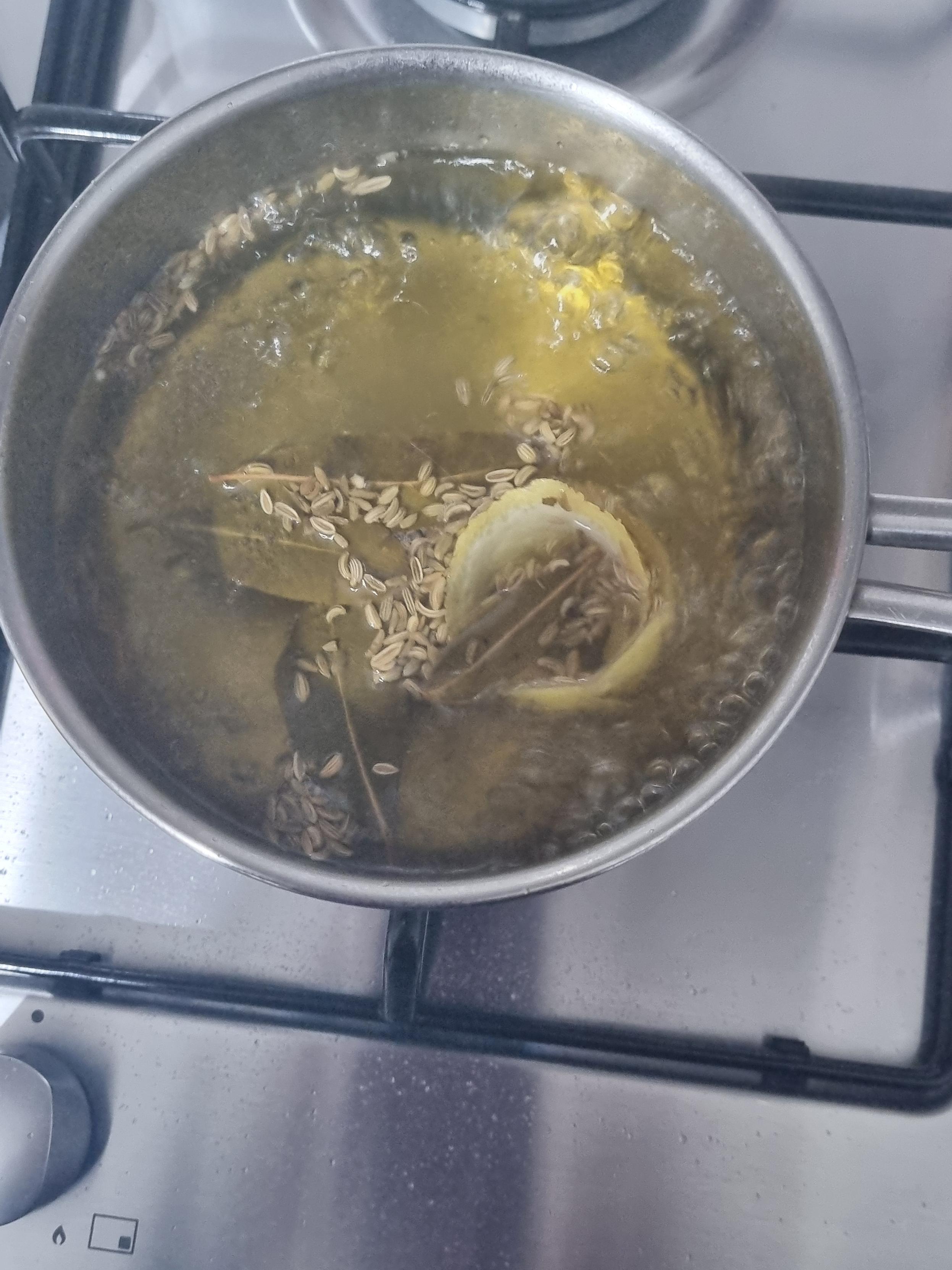 Pentolino con acqua in ebollizione, con buccia di limone, foglie di alloro e semi di finocchio