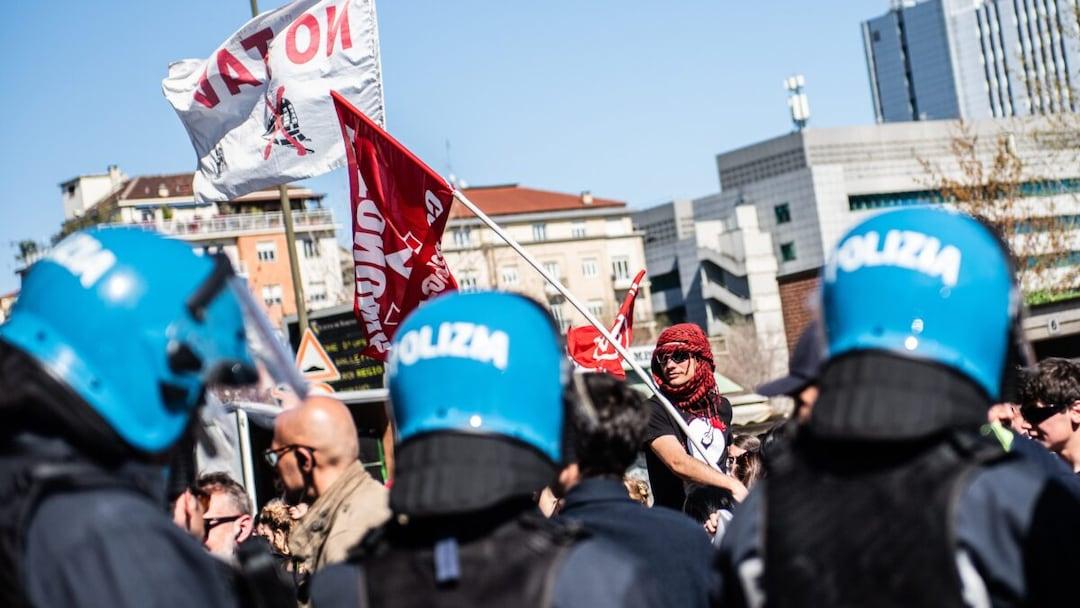 Nella fotografia, alcuni manifestanti No Tav sfilano di fronte ad un presidio della polizia.