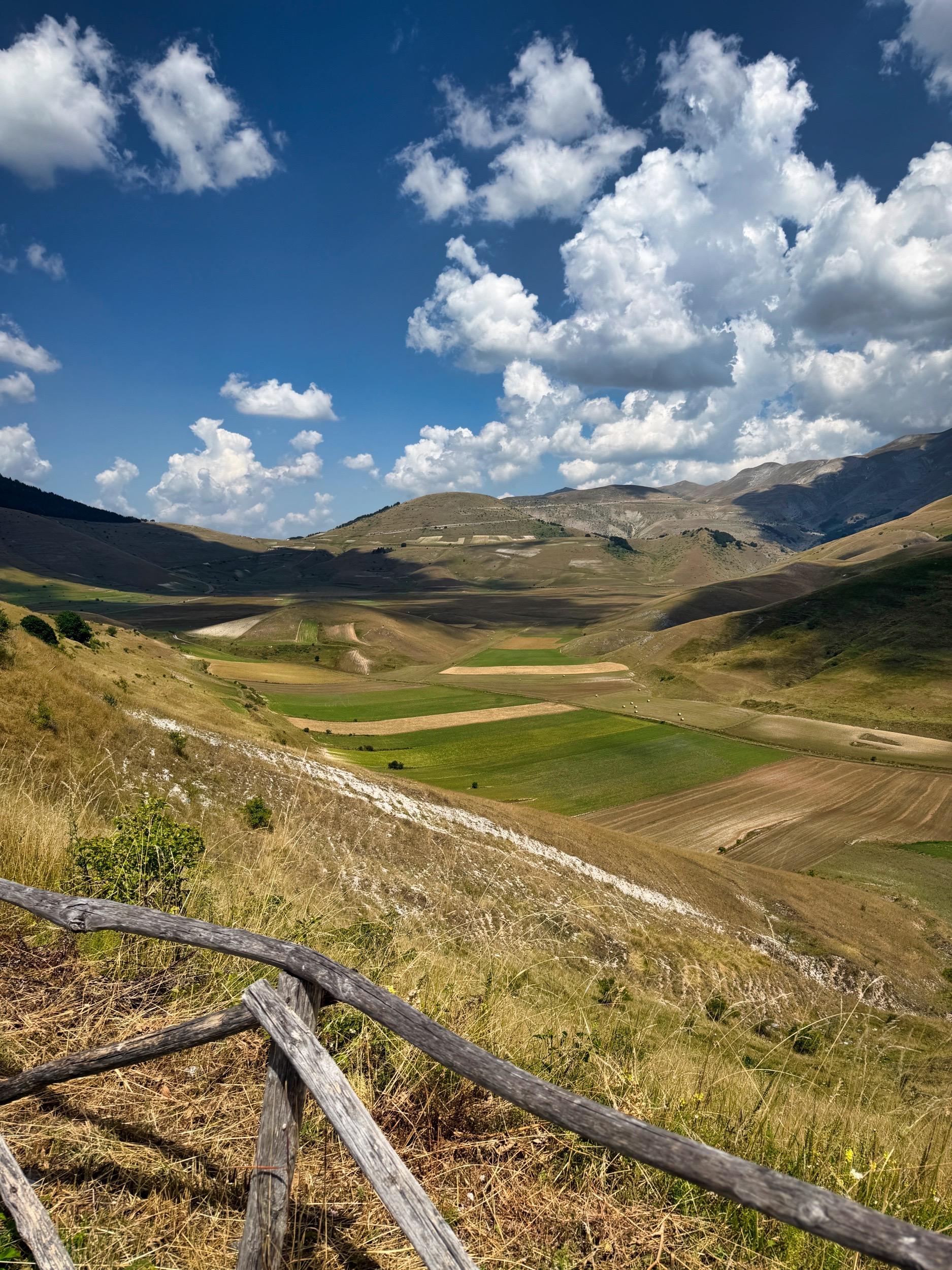 Castelluccio
Paesaggio montano con campi verdi, colline e cielo con nuvole bianche.