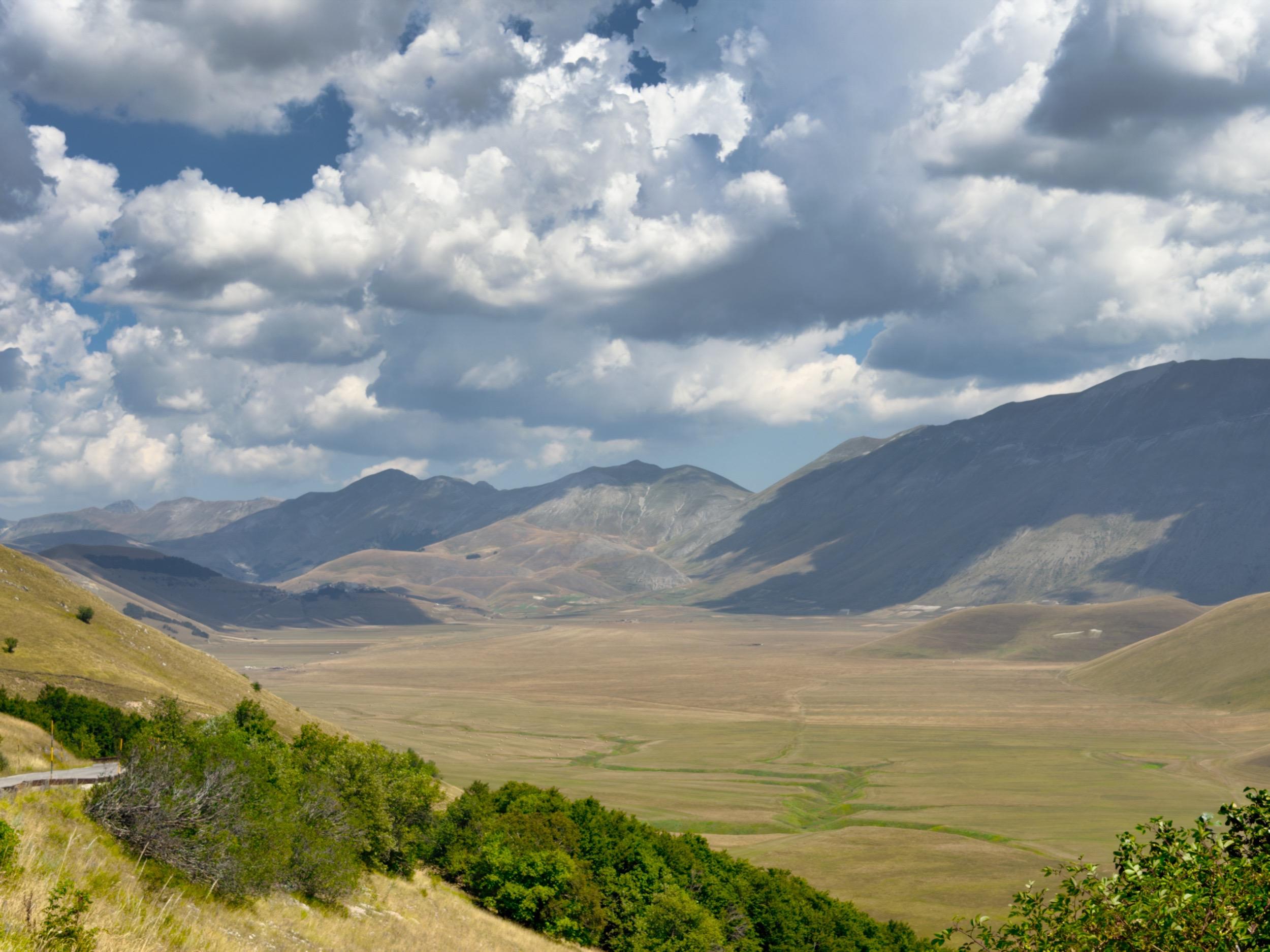 Castelluccio
Paesaggio di montagne e vallate sotto un cielo nuvoloso, con vegetazione verde e campi aperti in primo piano.