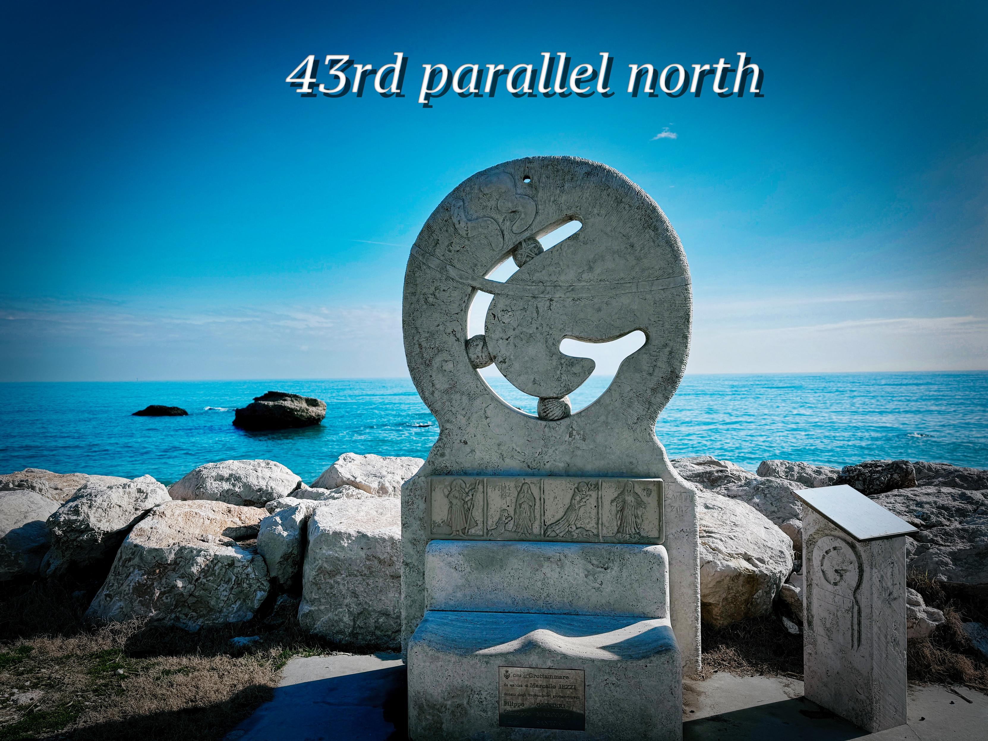 Scultura di pietra vicino al mare con scritta "43rd parallel north" in alto.