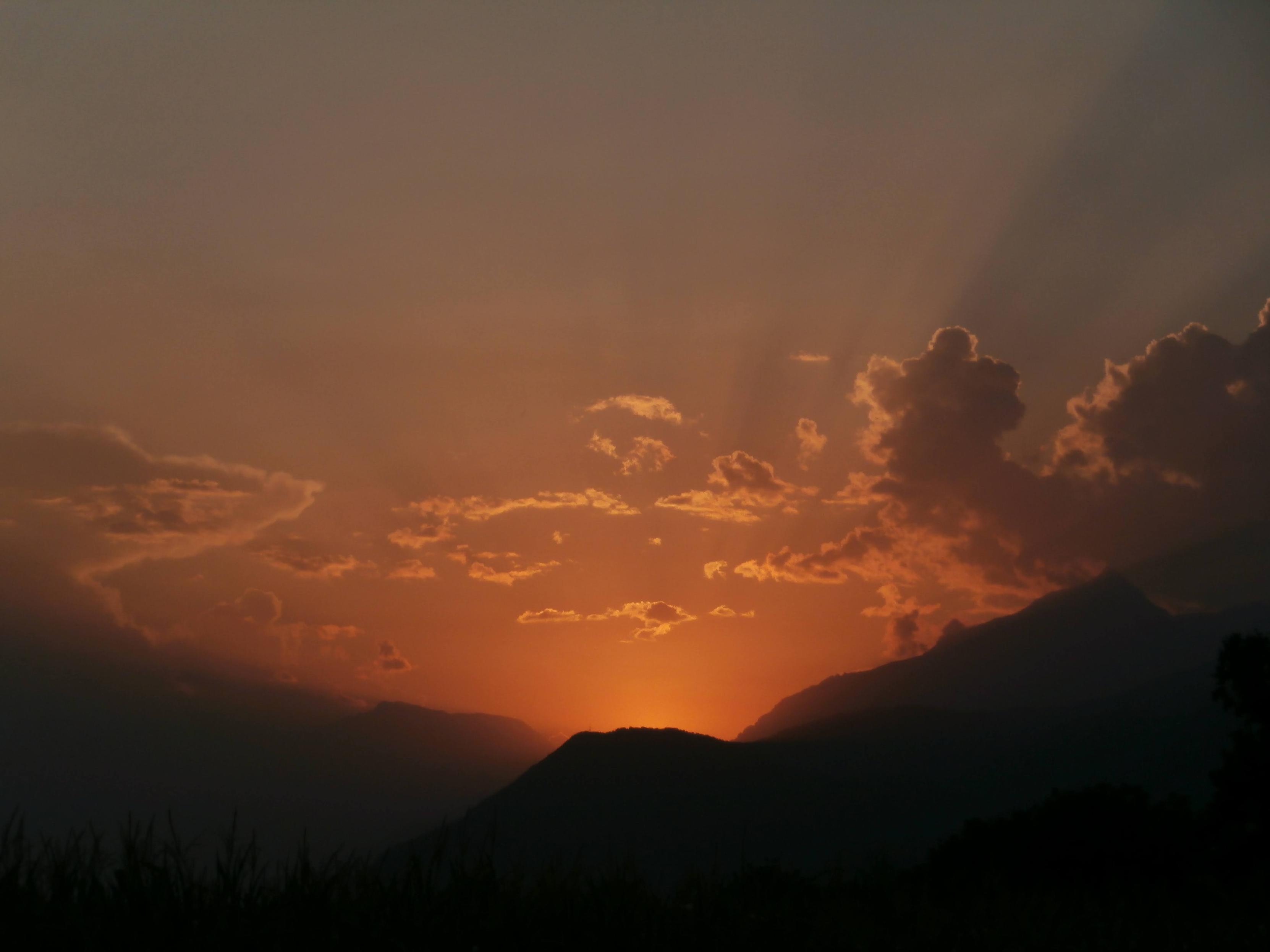 Il tramonto dell'eclisse.
Il sole non è più visibile. Si intuiscono i profili scuri delle montagne. La forte luce arancione scalda il cielo nuvoloso.