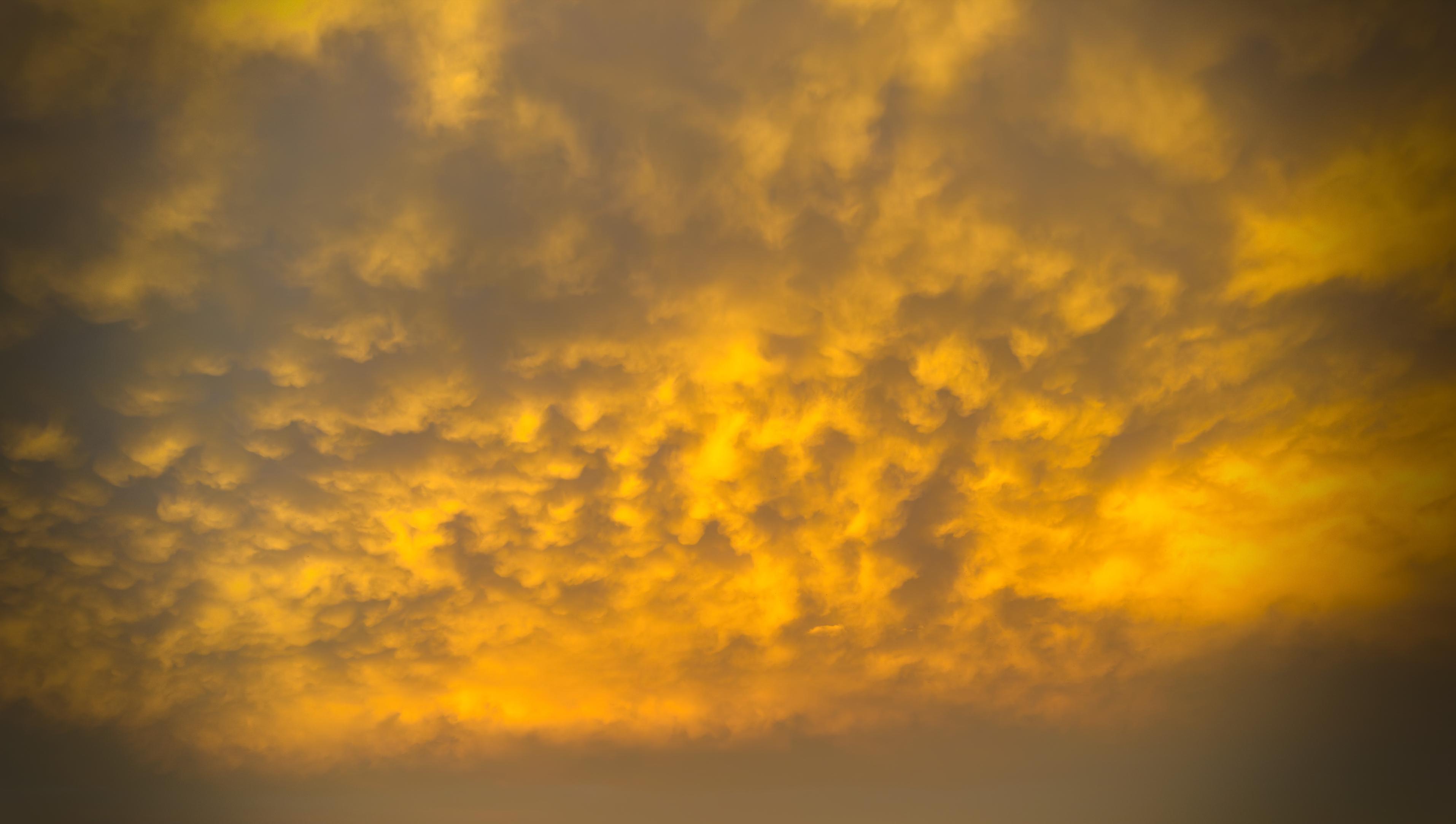 Cielo nuvoloso con tonalità calde gialle e arancioni al tramonto.