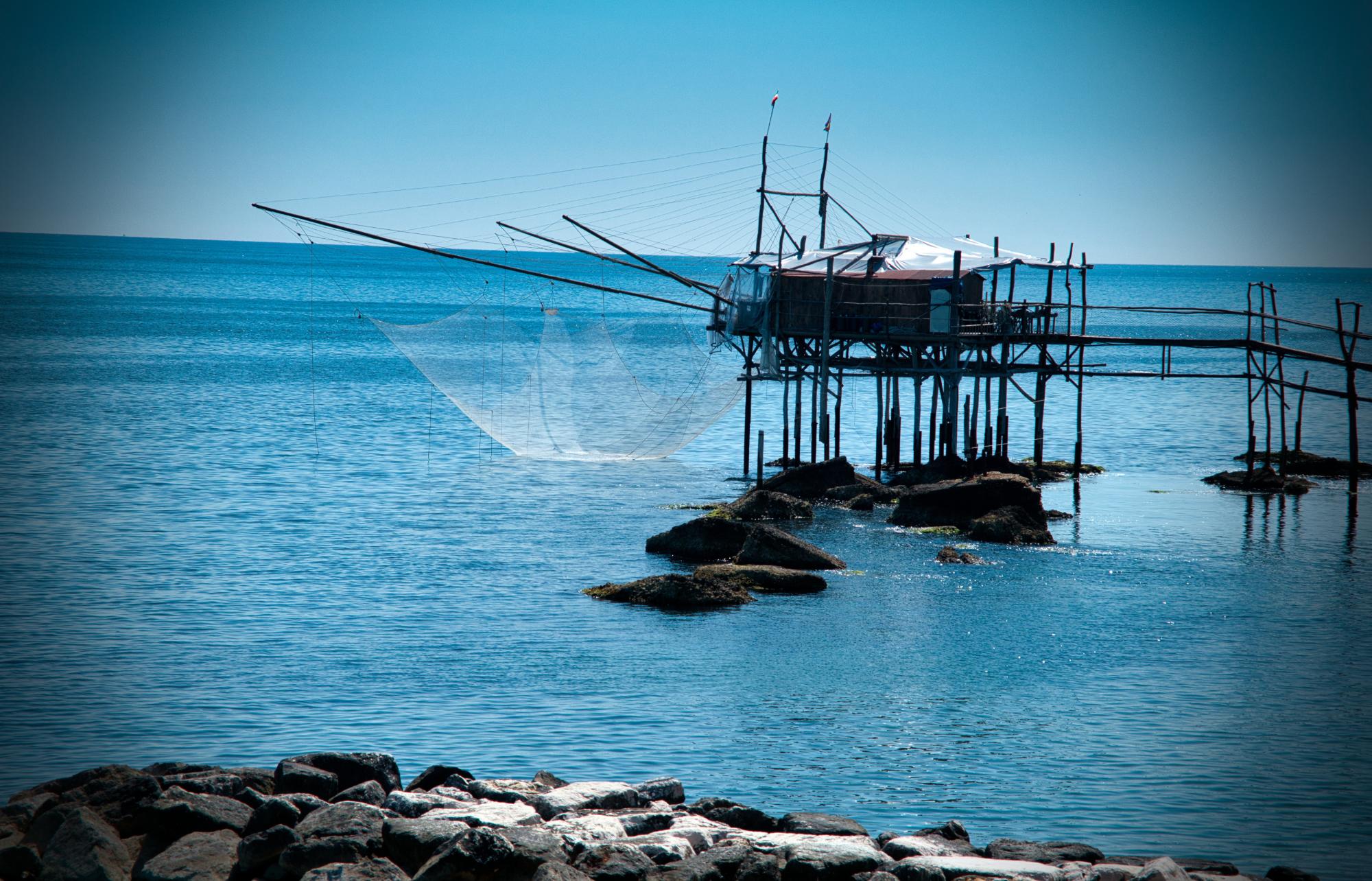 Trabocco di pescatori su alcune rocce, lungo la costa sul mare calmo e azzurro.