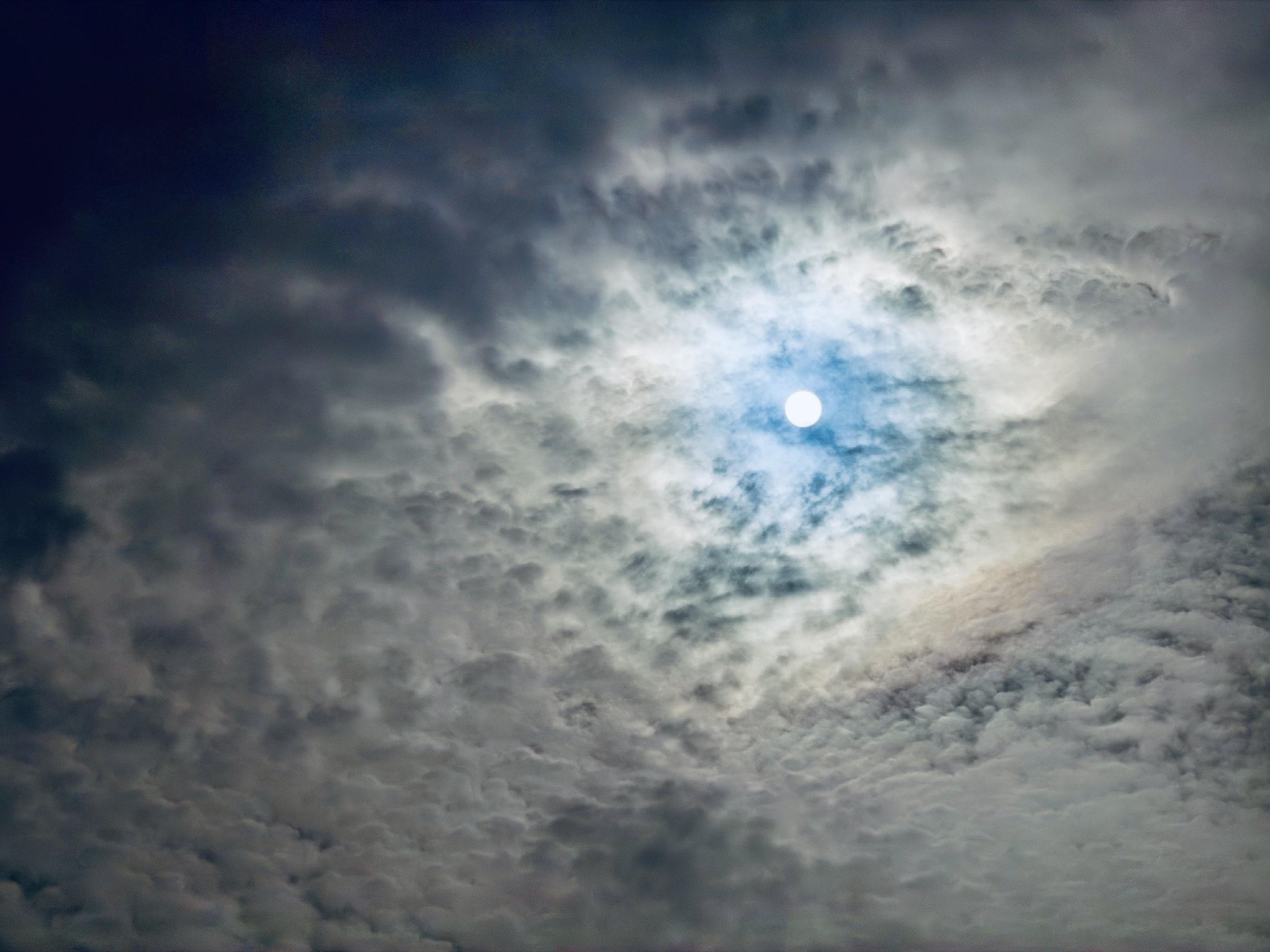Sole nascosto tra le nuvole, illuminata da un alone bluastro in un cielo nuvoloso.