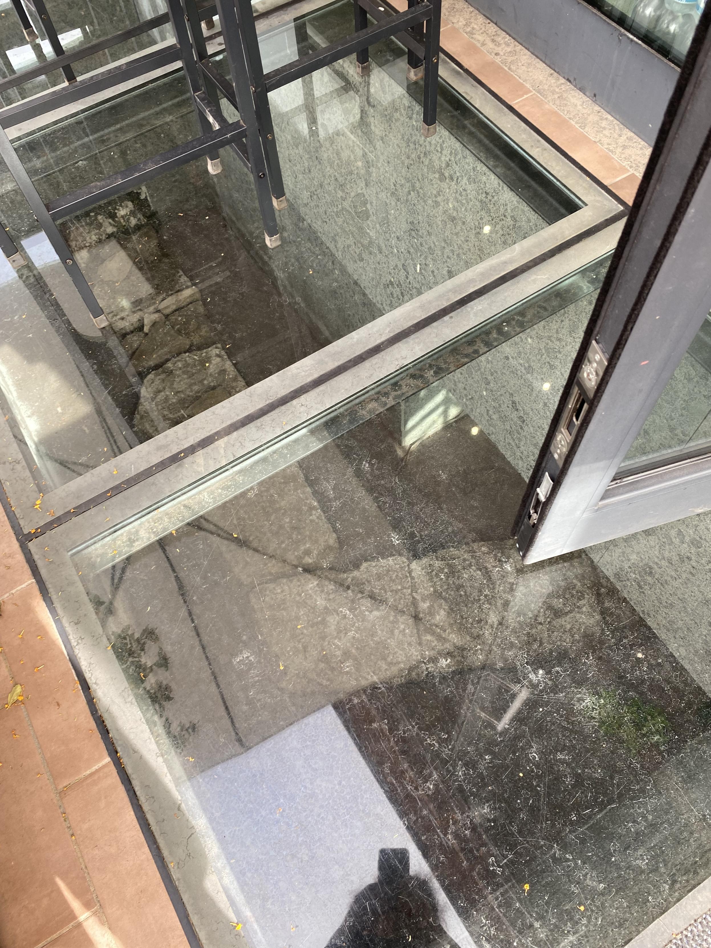An old wall is visible through a glass floor