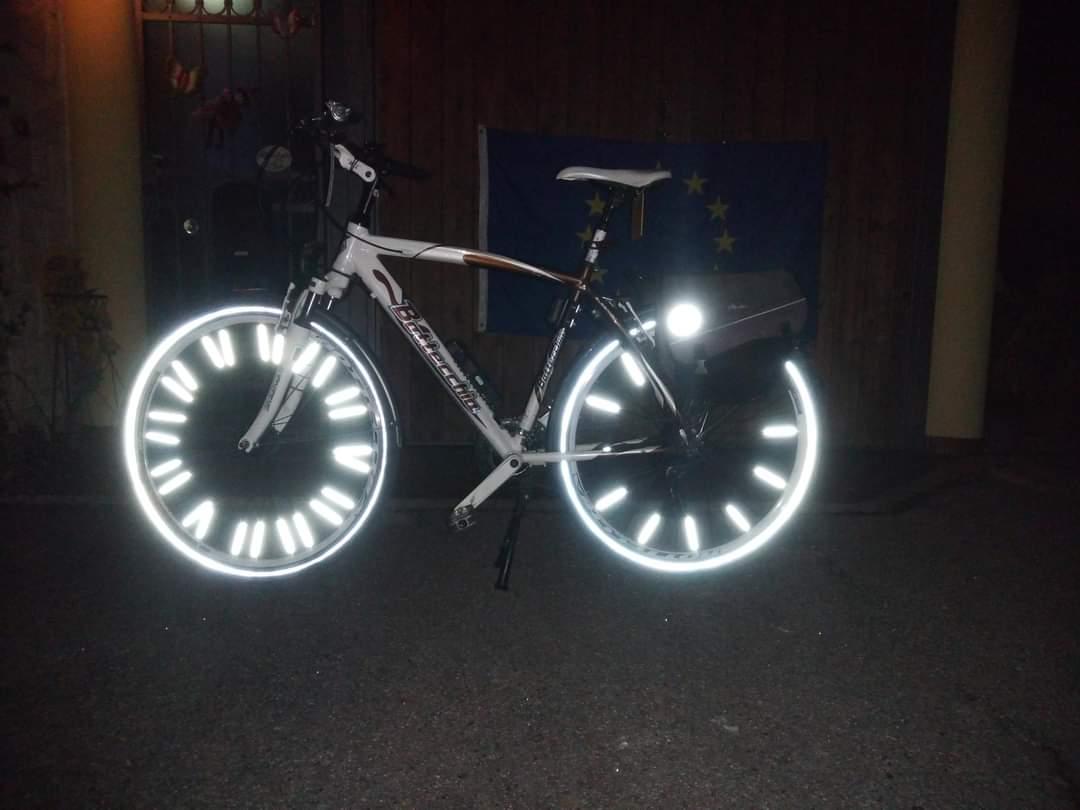 Bicicletta bianca/marrone di marchio Bottecchia. La foto è notturna e grazie al flash le bande riflettenti su ruote, raggi e borse splendono particolarmente forte.