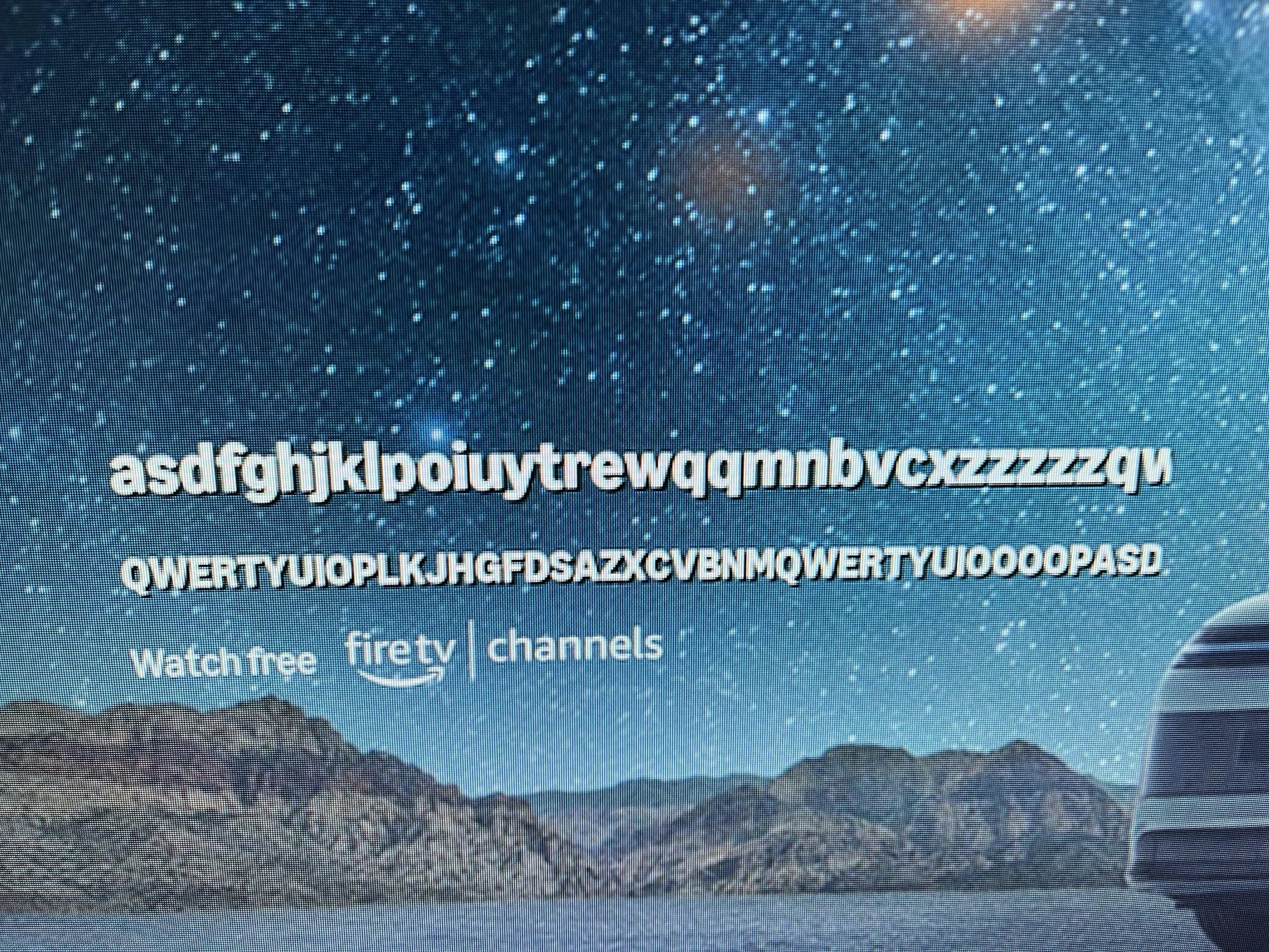 The image displays random keyboard faceroll text and a promotional message for "Watch free on Fire TV channels" against a starry night background with mountains.