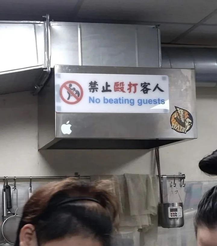 Sign above a kitchen ventilation area in Chinese and English: "No beating guests". Image of a stick figure giving a knee to the face of another stick figure with a red circled diagonal line across it