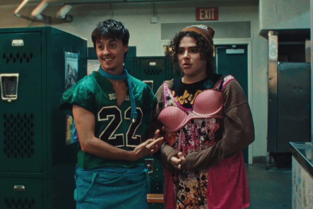 two high school kids stand in a locker room wearing hastily thrown on womens clothes