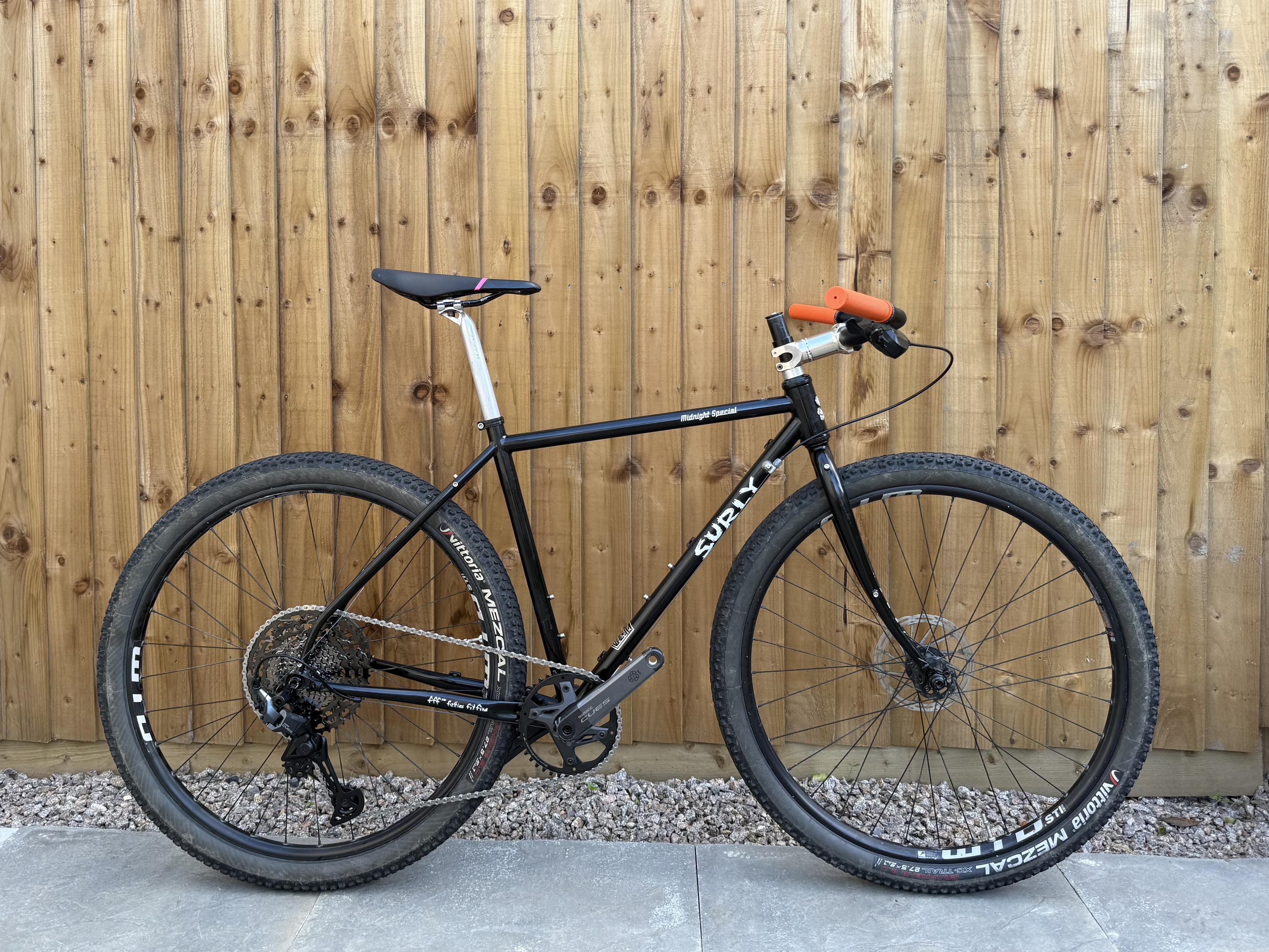 Work-in-progress bike build. A small black surly midnight special frame with silver seatpost and stem and orange grips. Wheels have mezcals fitted. There are no brakes yet.