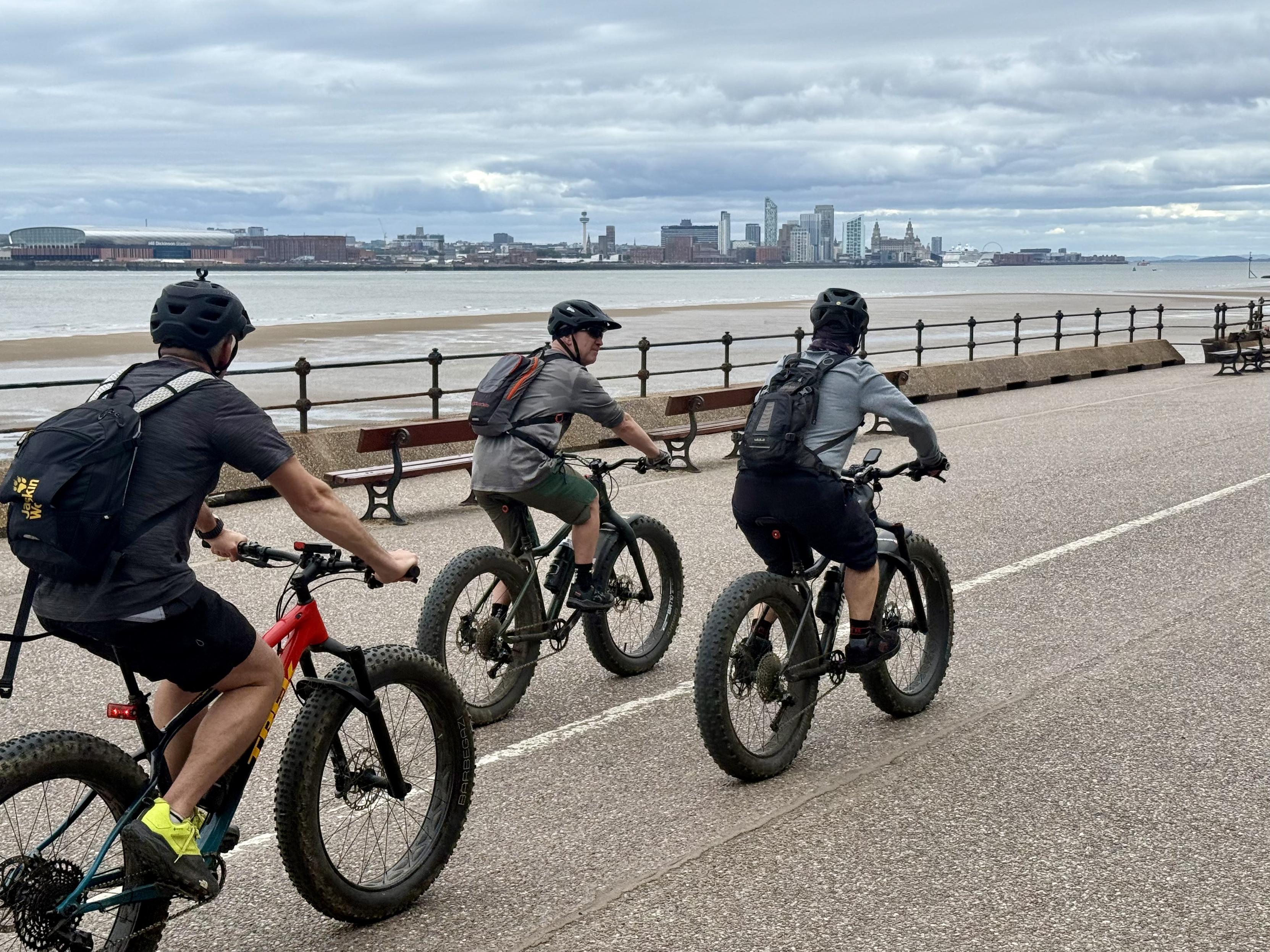 Three cyclists with Liverpool skyline in background across the Mersey