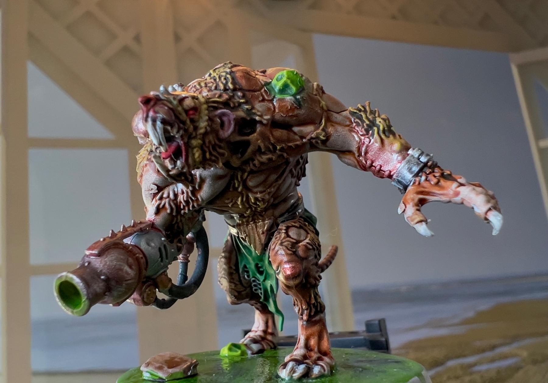 A detailed model of a mutant creature with mechanical elements and a large weapon stands in a dynamic pose against a blurred background.