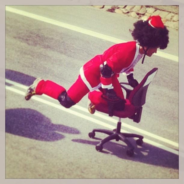 a man in a santa outfit and wig riding an office chair down hill at high speed
