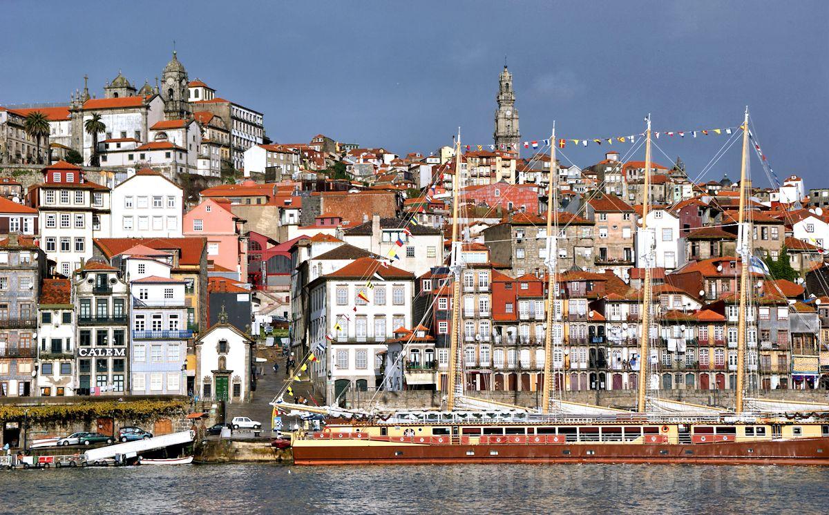 Vista da Ribeira, no Porto, com embarcação tradicional em primeiro plano e edifícios históricos alinhados na encosta.