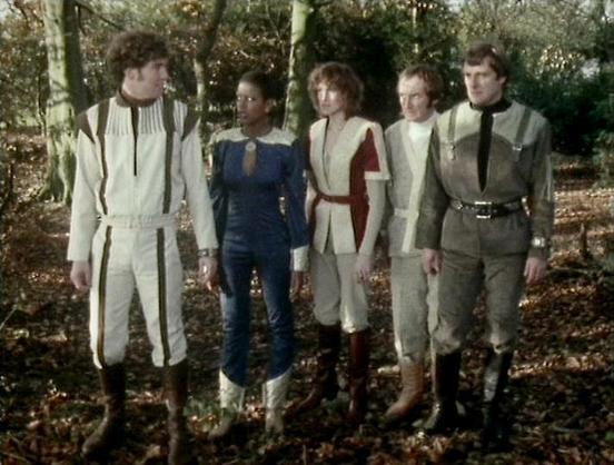 ChatGPT4 describes the image as: "The image shows a group of five people standing together in a forest setting during what appears to be autumn, as evidenced by the fallen leaves on the ground. They are dressed in futuristic or sci-fi-themed costumes, suggesting a scene from a television show or film. The clothing features distinctive styles and patterns typical of a speculative or space-themed setting.

The individuals are closely grouped, looking in the same direction, possibly engaged in con…