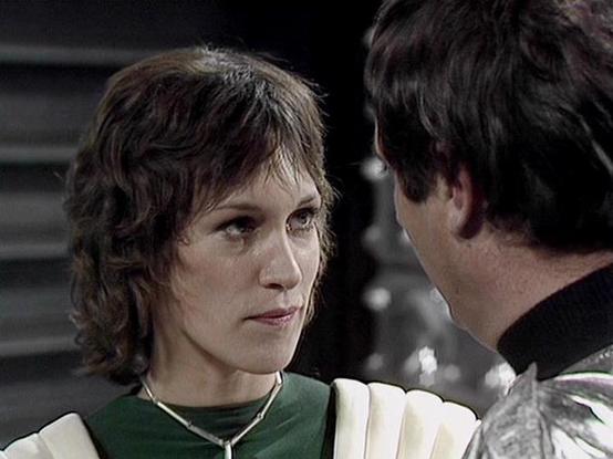 Claude Sonnet 4.0 describes the image as: "I can see this appears to be a scene from a science fiction television series, showing two characters in what looks like a futuristic or spacecraft setting. One character is wearing a green outfit and has curly hair, while the other is wearing darker clothing. The lighting and production style suggests this is from a British science fiction show, likely from the late 1970s or early 1980s based on the visual aesthetic. The scene appears to show an intim…