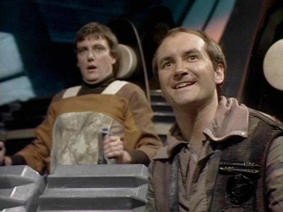 Claude 3.7 describes the image as: "This appears to be a scene from a classic science fiction television series, set in what looks like a spacecraft or control room. The image shows two people seated in a futuristic cockpit or command area. One person on the left wears a brown and beige outfit, while the person on the right has a lighter brownish jacket with some distinctive details. The setting has the distinctive retro-futuristic aesthetic typical of British sci-fi productions from the late 1…