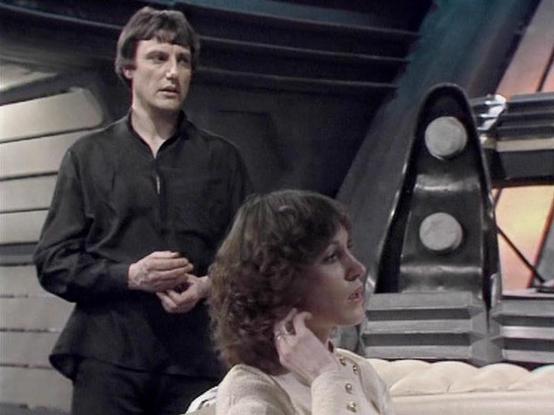 Claude Sonnet 4.0 describes the image as: "I can see this appears to be from a science fiction television series, showing two people in what looks like a futuristic spacecraft interior. The setting features typical sci-fi production design with metallic surfaces, control panels, and angular architectural elements characteristic of 1970s-80s television production values.

One person is wearing dark clothing and standing, while another is seated wearing lighter colored clothing. The scene appears…