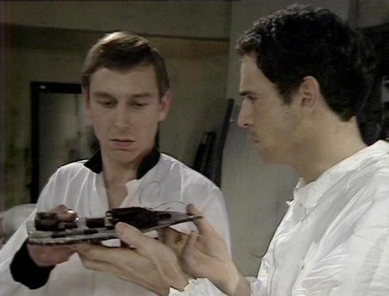 Claude Sonnet 4.0 describes the image as: "I can see two people in white clothing in what appears to be a clinical or medical facility setting. One person is holding what looks like a dark-colored medical or scientific instrument or device, showing it to the other person. The environment has the sterile, institutional appearance typical of a medical facility or laboratory, with neutral-colored walls and clinical lighting. Both individuals appear to be examining or discussing the device, suggest…
