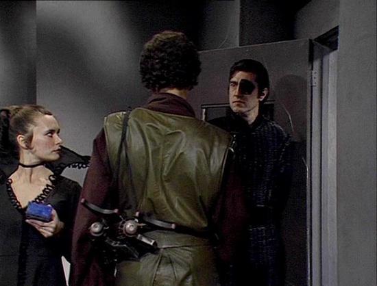 Claude Sonnet 4.0 describes the image as: "This appears to be a tense scene set in what looks like a spacecraft or space station corridor. The setting has the characteristic sterile, industrial aesthetic typical of science fiction productions from this era, with gray walls and functional lighting.

In the scene, there are three figures - one person wearing a distinctive olive-green uniform with a belt and equipment, suggesting they may be a guard or security officer. They appear to be confronti…