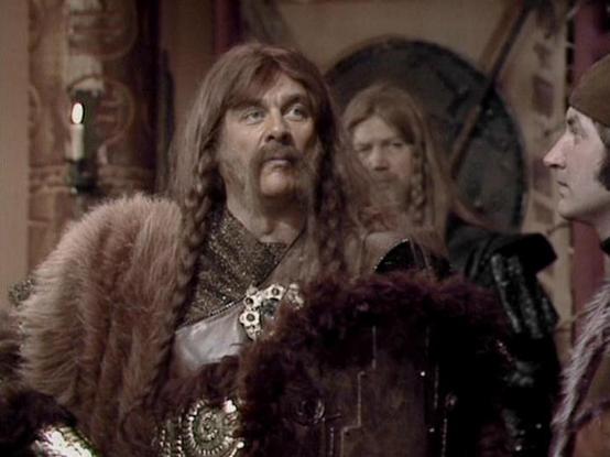 Claude Sonnet 4.0 describes the image as: "I can see this appears to be from a science fiction television series, showing what looks like a dramatic scene with characters in period or fantasy-style costumes. The setting appears to be indoors with ornate decorative elements visible in the background. The characters are wearing elaborate clothing with metallic details and fur trim, suggesting this might be from an episode with a historical or fantasy theme. The lighting and production style is ch…