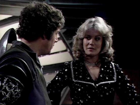 Claude Sonnet 4.0 describes the image as: "I can see this appears to be from a science fiction television series, showing two characters in what looks like a spacecraft or futuristic setting. One character is wearing dark clothing and has curly dark hair, while the other has blonde/light colored hair and is wearing a distinctive black outfit with metallic studs or decorative elements and what appears to be silver trim. The setting has the characteristic look of 1970s sci-fi production design, w…