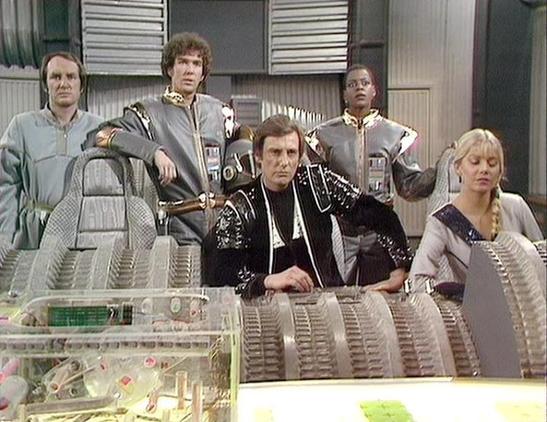 Claude 3.7 describes the image as: "This image shows a scene from a science fiction television series, set in what appears to be a futuristic spacecraft control room or command center. The characters are seated and standing around a console with technical equipment visible in the foreground.

The individuals are wearing distinctive 1980s-style sci-fi costumes - some in metallic gray uniforms with gold accents on the shoulders, while the central figure wears a more elaborate black outfit with de…