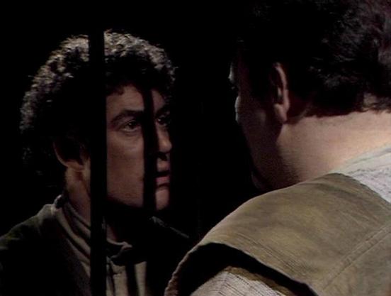 Claude Sonnet 4.0 describes the image as: "I can see this appears to be a dramatic scene with two male characters in what looks like a dimly lit, confined space - possibly aboard a spacecraft or in some kind of underground facility. The lighting creates strong shadows across their faces, giving the scene a tense, serious atmosphere. One character is facing toward the camera while engaged in what appears to be an intense conversation or confrontation with the other character, whose back is parti…
