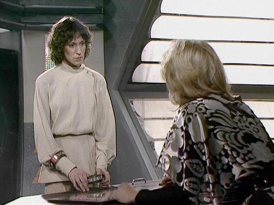 Claude Sonnet 4.0 describes the image as: "I can see this is a scene set in what appears to be a spacecraft interior, with characteristic futuristic design elements including curved walls and sleek surfaces. Two women are present in the scene - one wearing a light-colored, flowing garment with a belt, and another in a patterned outfit. The setting has the distinctive aesthetic of late 1970s science fiction television, with clean lines and a sterile, high-tech atmosphere. The scene appears to be…