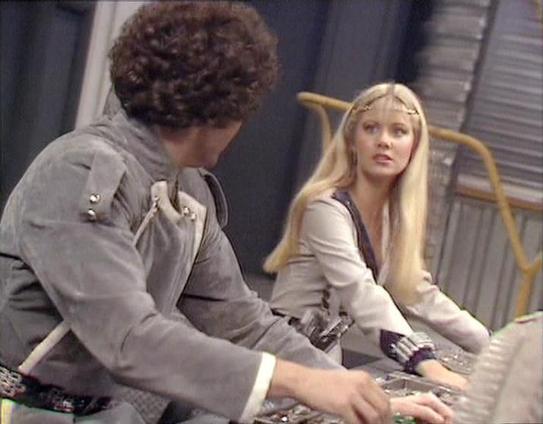 Claude 3.7 describes the image as: "The image shows a scene from a science fiction television production, appearing to be from the late 1970s or early 1980s based on the styling and production quality. 

Two people are shown in what looks like a spacecraft or futuristic control room. On the left is a person with curly dark hair wearing a gray uniform with decorative elements at the shoulders. On the right is someone with long blonde hair in a similar styled uniform with dark accents.

Both appe…