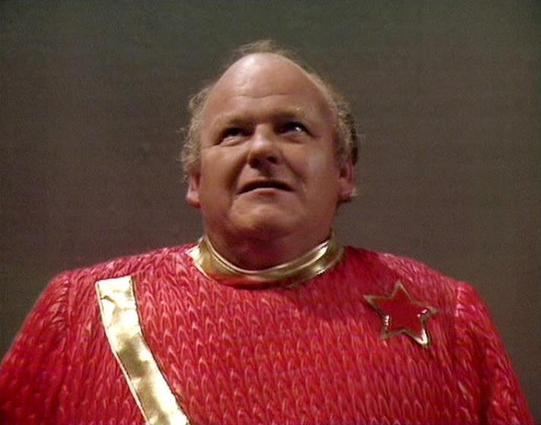 Claude Sonnet 4.0 describes the image as: "I can see this appears to be from a science fiction television production, showing someone wearing an elaborate red costume with a distinctive scaled or textured pattern and gold collar details. The costume design suggests this is from a futuristic or fantasy setting, with the ornate styling typical of ceremonial or high-ranking character attire in classic sci-fi productions. The lighting and image quality are characteristic of television productions f…
