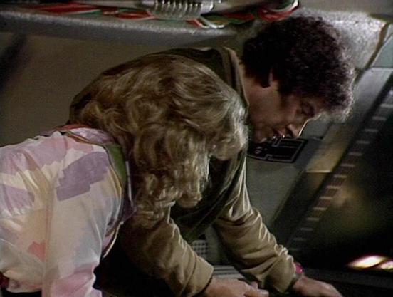 Claude 3.7 describes the image as: "This image appears to be from a science fiction television series from the late 1970s or early 1980s. The scene takes place on what looks like a spacecraft control room or console area. Two people are shown leaning over what appears to be a control panel or computer terminal. One person has blonde wavy hair and is wearing a pastel-colored striped shirt, while the other has dark curly hair and is wearing what appears to be a tan or beige outfit. They seem to b…