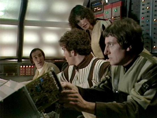 Claude 3.7 describes the image as: "This image appears to be from a vintage science fiction television production, showing a control room or spacecraft bridge setting. Several individuals are gathered around what looks like technical equipment or control panels. The scene has the distinctive aesthetic of classic sci-fi from the late 1970s or early 1980s, with retro-futuristic technology featuring blinking lights and circuit boards visible in the foreground.

The setting appears to be a technica…