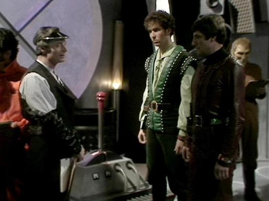 Claude 3.7 describes the image as: "This image shows a scene from a science fiction television series, featuring several performers in a futuristic setting. The scene takes place in what appears to be a spacecraft or space station interior with distinctive curved walls and technical equipment visible.

Three main figures are prominent in the frame - one wearing a cap and light-colored shirt with a dark vest on the left, another in a green leather-like outfit with studded detailing in the center…