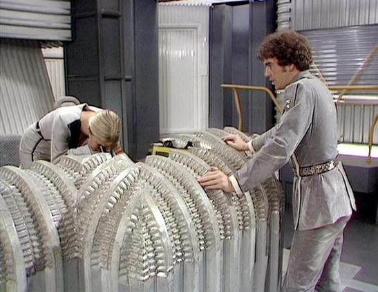 Claude 3.7 describes the image as: "This image shows a scene set in what appears to be a futuristic or sci-fi environment with metallic walls and technical equipment. Two people are examining or working with a large mechanical structure that has a ribbed or segmented design. One person with blonde hair is leaning over the structure while another person in a gray uniform-like outfit with a belt is standing and handling part of the mechanism.

The setting has the distinctive retro sci-fi aestheti…
