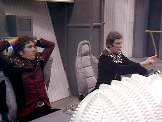 Claude 3.7 describes the image as: "The image shows two people in what appears to be a spacecraft control room or flight deck. On the left, a person wearing a burgundy/red outfit with dark curly hair is leaning back with hands behind their head. On the right, another person in a dark jacket with a patterned collar is pointing at something, seemingly operating controls.

In the foreground, there's a white, circular control panel or console with textured, ridge-like patterns. The set has a distin…