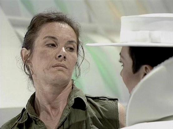 Claude Sonnet 4.0 describes the image as: "I can see this appears to be from a science fiction television production, showing what looks like a medical or laboratory setting. There's a person in what appears to be a green/olive colored uniform or medical garment, and another figure in white (possibly medical attire) in the background. The setting has a clinical, futuristic appearance with clean white surfaces and lighting typical of sci-fi medical facilities. However, I cannot identify the spec…