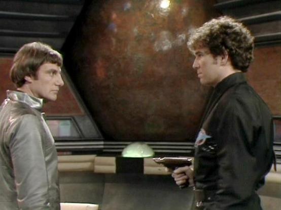 Claude Sonnet 4.0 describes the image as: "I can see this is a scene set in what appears to be a spaceship interior, with a large viewscreen or window showing space in the background. The setting has a futuristic control room or bridge aesthetic typical of science fiction productions from this era, with control panels and seating areas visible. The two figures are positioned facing each other in what seems to be a tense conversational moment, with one wearing what appears to be a light-colored …