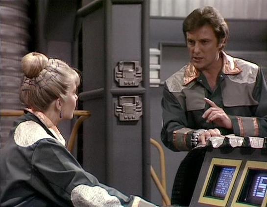 Claude Sonnet 4.0 describes the image as: "This appears to be a scene set in a futuristic spacecraft or space station interior. The setting features typical sci-fi elements including control panels with digital displays and metallic walls. Two characters are shown in what appears to be a tense conversation or confrontation. The woman on the left has blonde hair styled in an updo and wears what looks like a light-colored top with dark outer garment. The man on the right wears a distinctive leath…